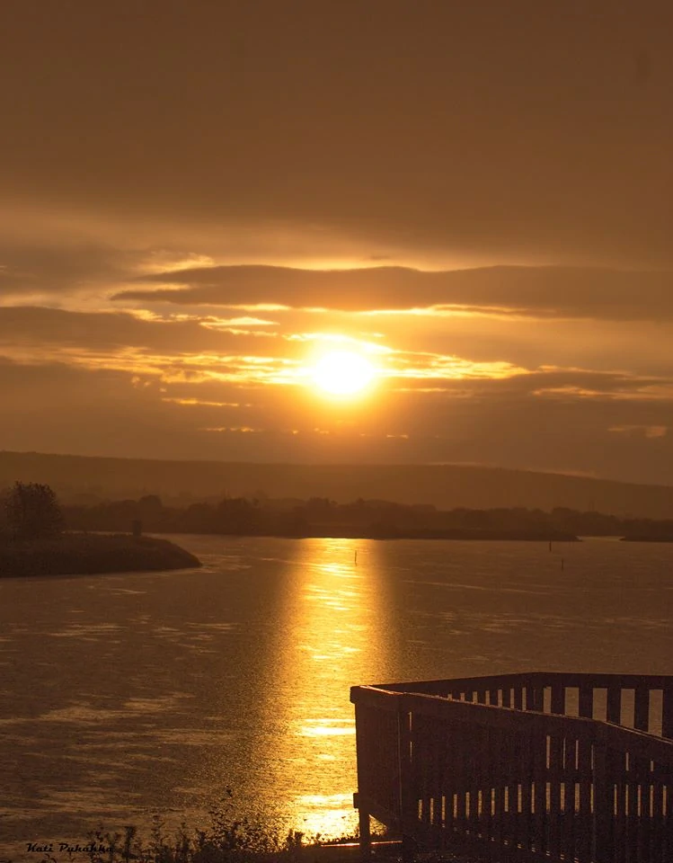 Auringonlasku heijastuu tyyneen järveen laiturilta katsottuna
